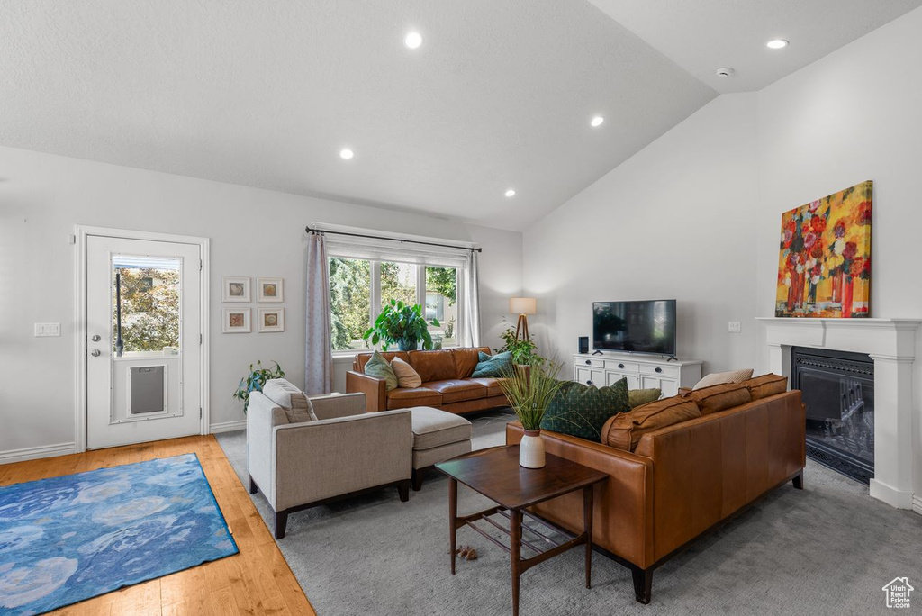 Living room with recessed lighting, a glass covered fireplace, wood finished floors, and high vaulted ceiling
