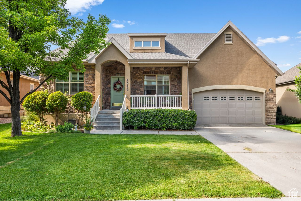 View of front of property with stone siding, driveway, a front lawn, stucco siding, and an attached garage