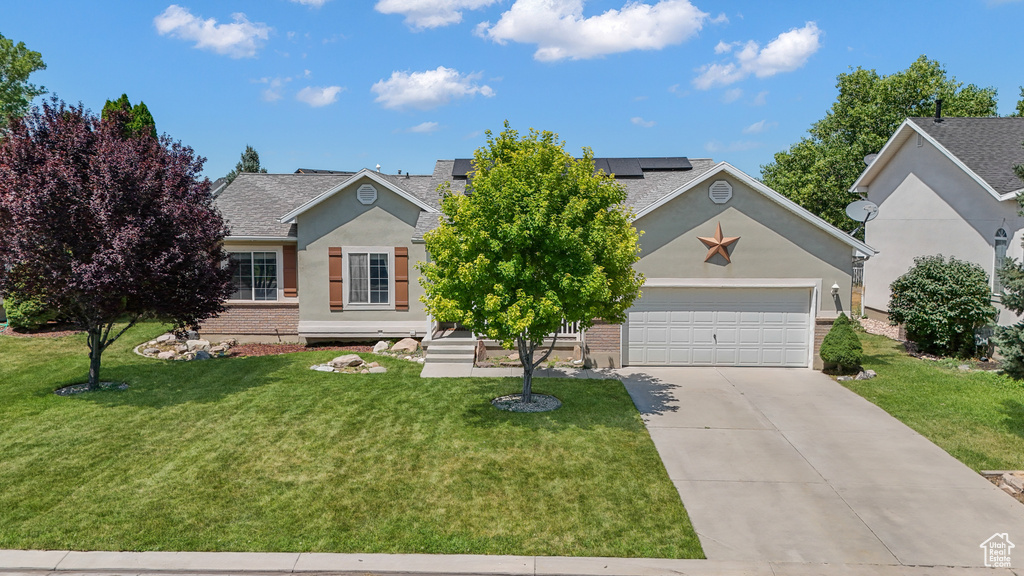 View of front facade with driveway, solar panels, brick siding, and a front lawn