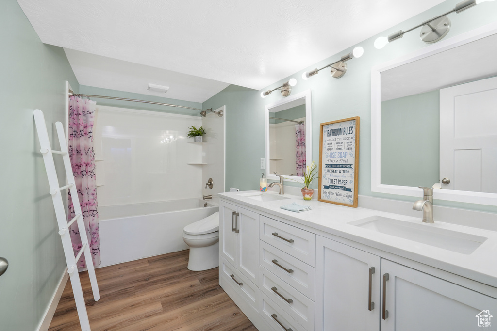 Bathroom with double vanity, shower / tub combo with curtain, and wood finished floors