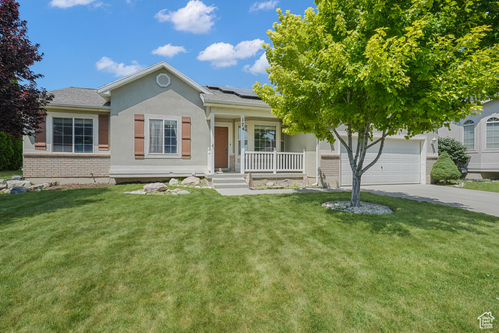 Ranch-style house with a porch, driveway, roof mounted solar panels, a garage, and stucco siding