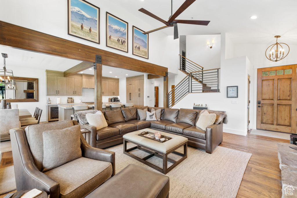 Living room with a chandelier, stairs, a ceiling fan, high vaulted ceiling, and light wood-style flooring