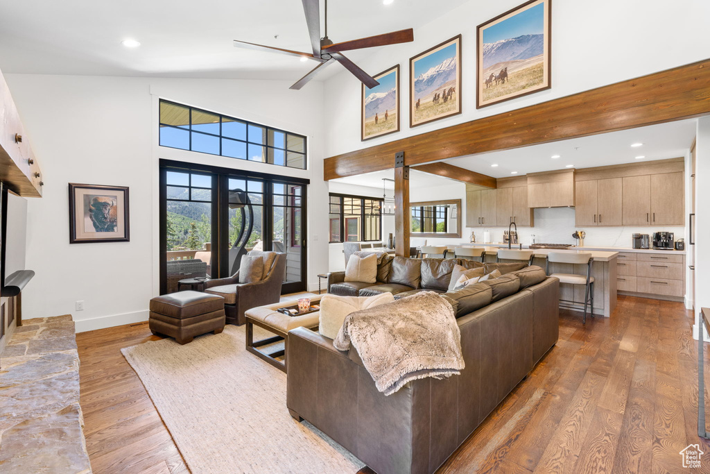 Living area with light wood-type flooring, a ceiling fan, recessed lighting, high vaulted ceiling, and beamed ceiling