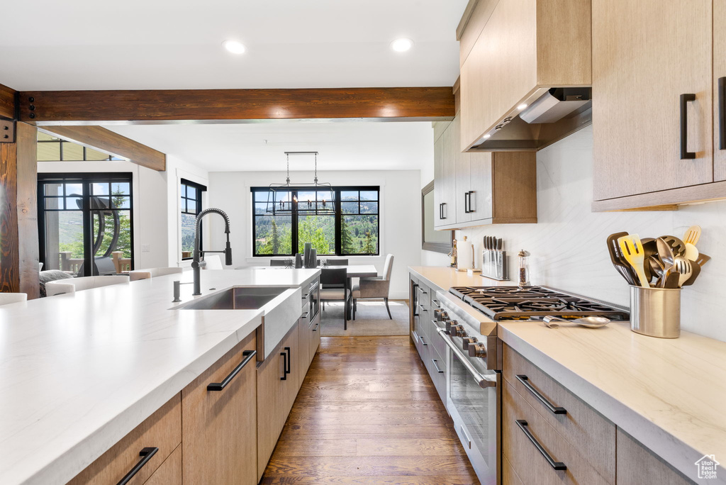 Kitchen featuring high end stainless steel range oven, beam ceiling, wood finished floors, light brown cabinetry, and tasteful backsplash