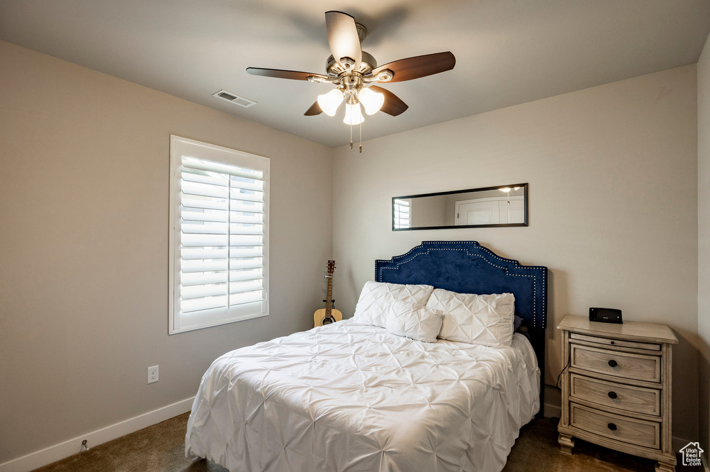 Bedroom with dark colored carpet, multiple windows, and ceiling fan