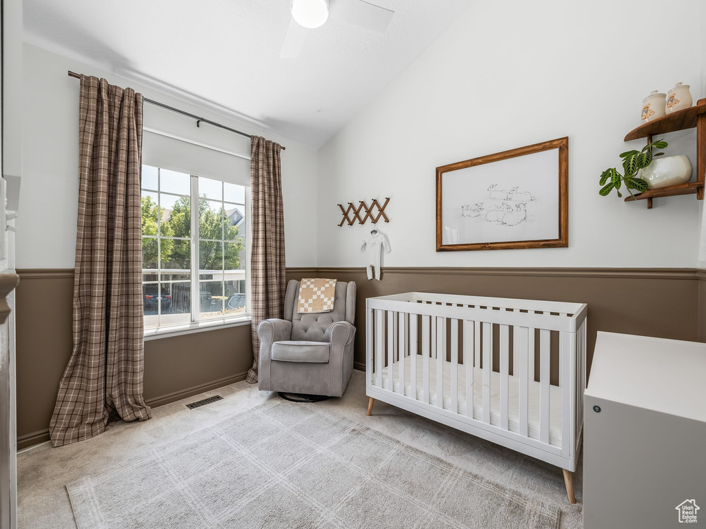 Carpeted bedroom featuring vaulted ceiling, a nursery area, and a ceiling fan