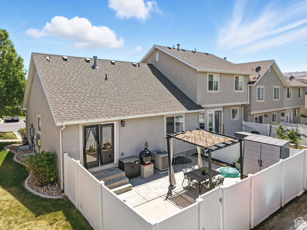 Rear view of house featuring stucco siding, roof with shingles, a fenced backyard, and a patio area