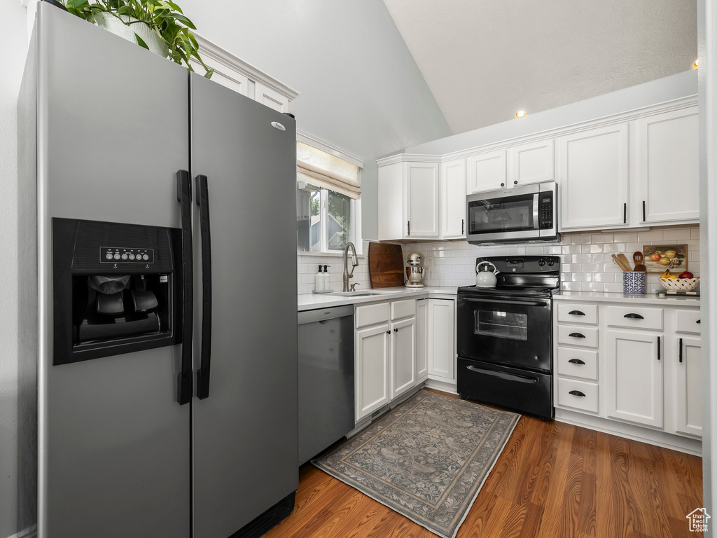 Kitchen with appliances with stainless steel finishes, light countertops, lofted ceiling, white cabinetry, and dark wood finished floors