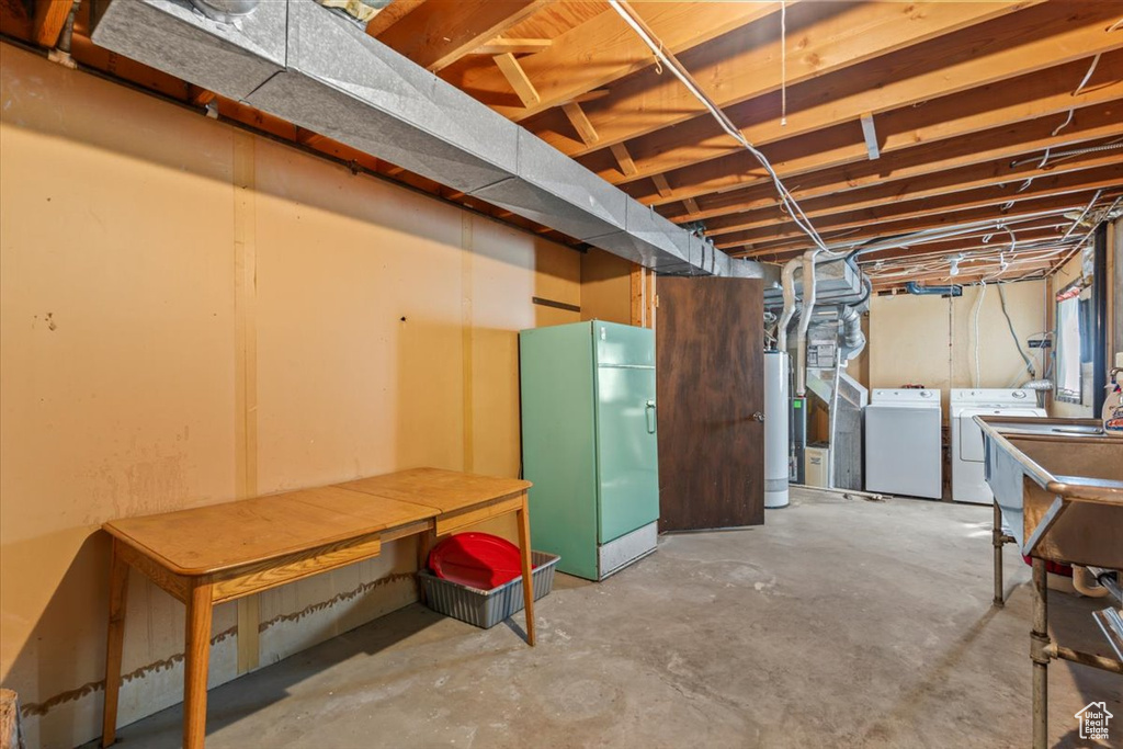 Unfinished basement featuring washer and dryer, freestanding refrigerator, and water heater