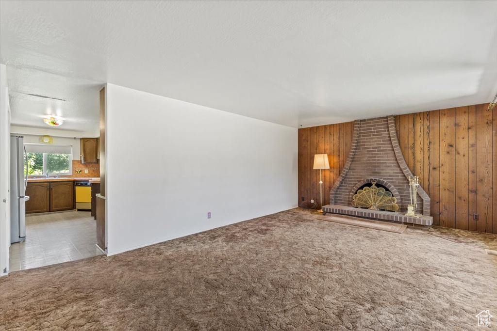 Unfurnished living room featuring wooden walls, light colored carpet, and a wood stove