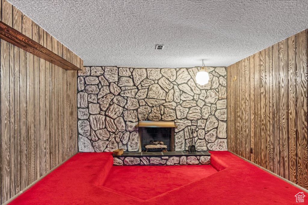 Unfurnished living room featuring wooden walls, a textured ceiling, carpet flooring, and a fireplace