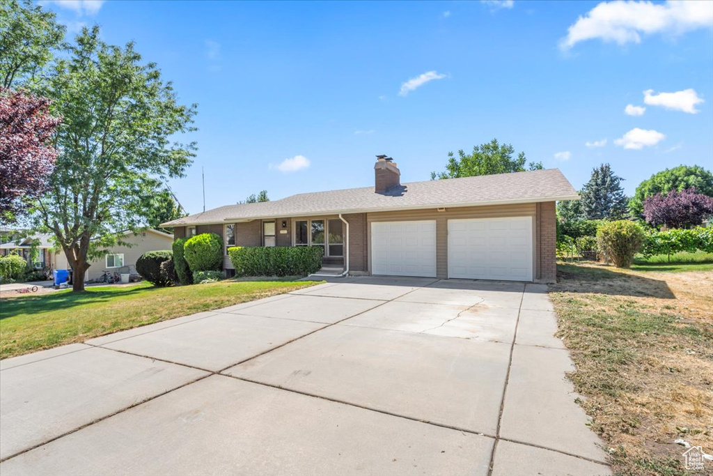 Ranch-style house featuring brick siding, an attached garage, driveway, a chimney, and a front lawn
