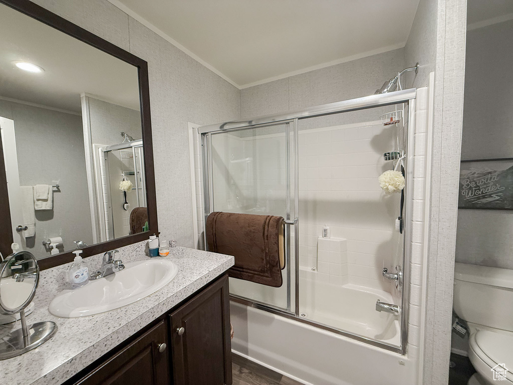 Full bath featuring ornamental molding, bath / shower combo with glass door, vanity, and wood finished floors