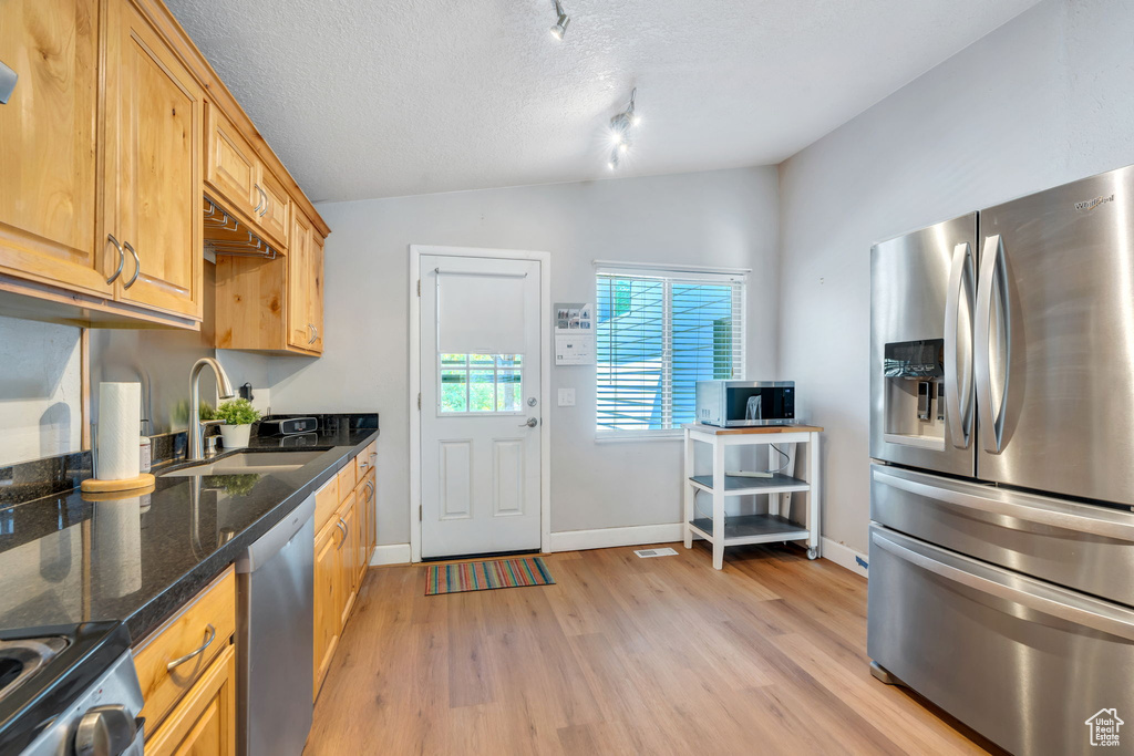 Kitchen featuring appliances with stainless steel finishes, lofted ceiling, light wood-style flooring, dark stone countertops, and a textured ceiling