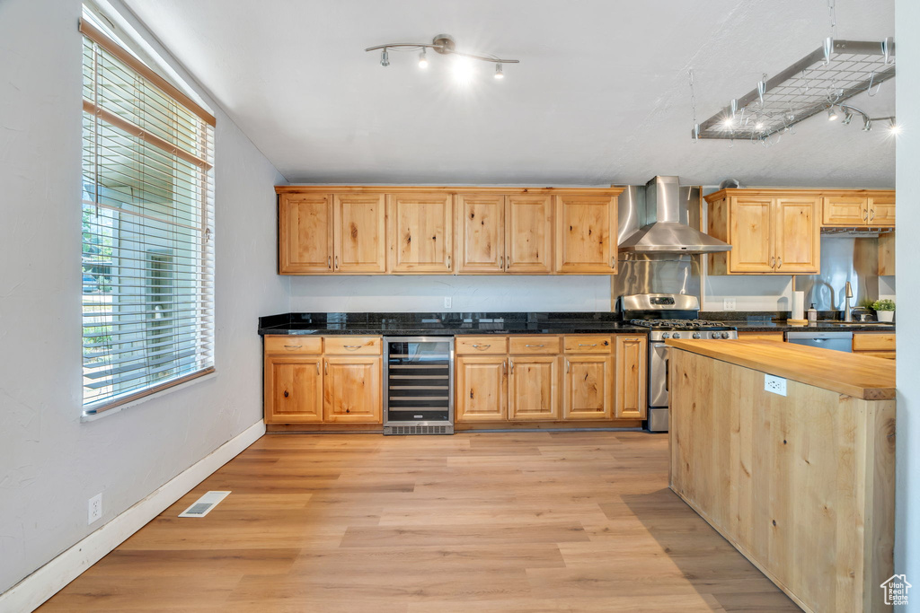 Kitchen with track lighting, beverage cooler, appliances with stainless steel finishes, wall chimney range hood, and light wood-style flooring