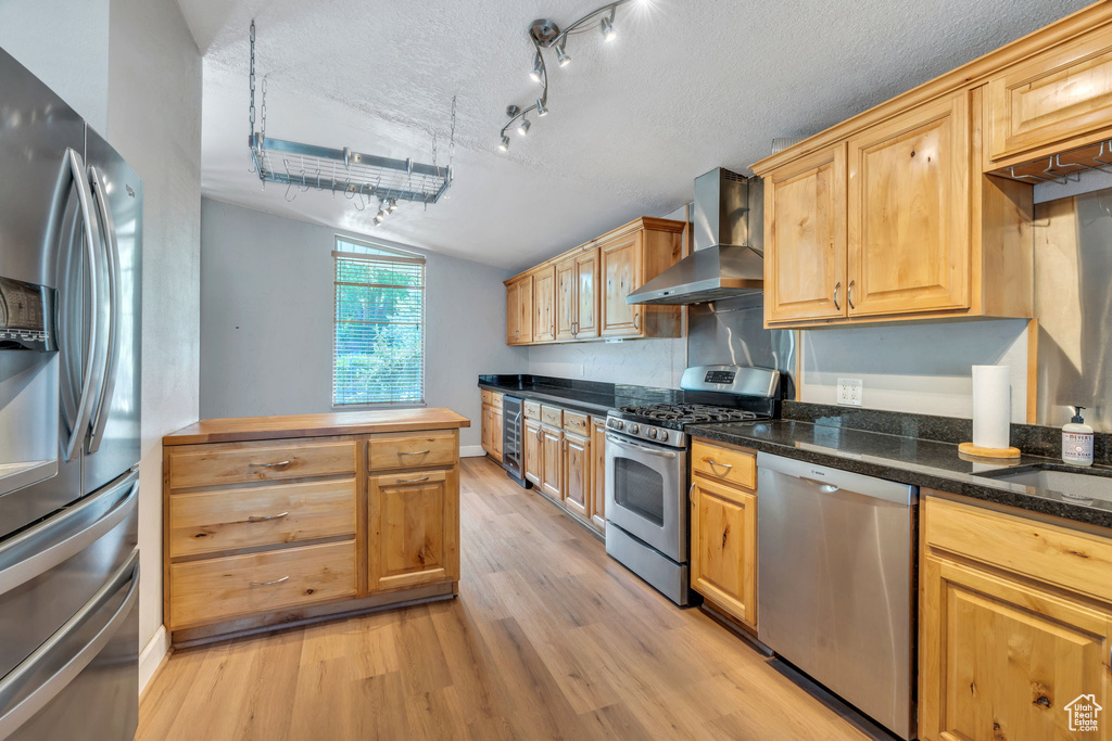 Kitchen with stainless steel appliances, light wood-style floors, wall chimney exhaust hood, lofted ceiling, and wine cooler