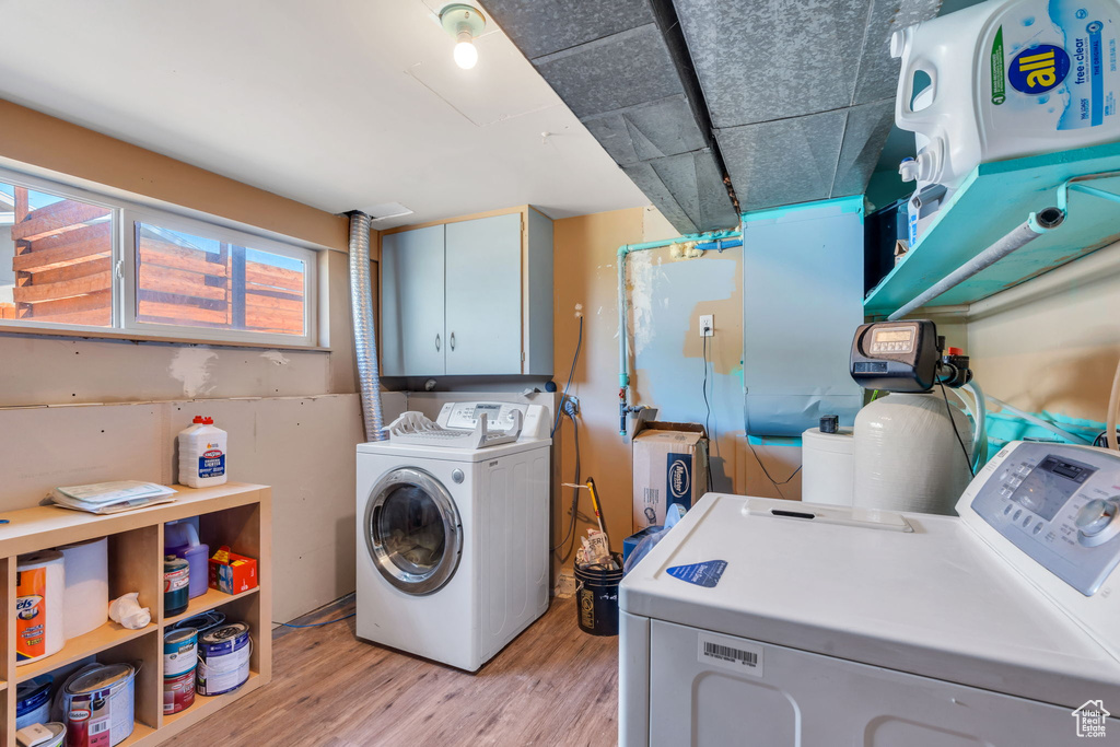 Laundry room with washer and dryer, light wood-type flooring, and cabinet space
