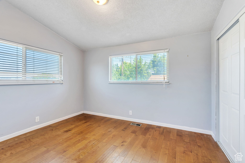 Unfurnished bedroom featuring a closet, lofted ceiling, a textured ceiling, and light wood-style floors