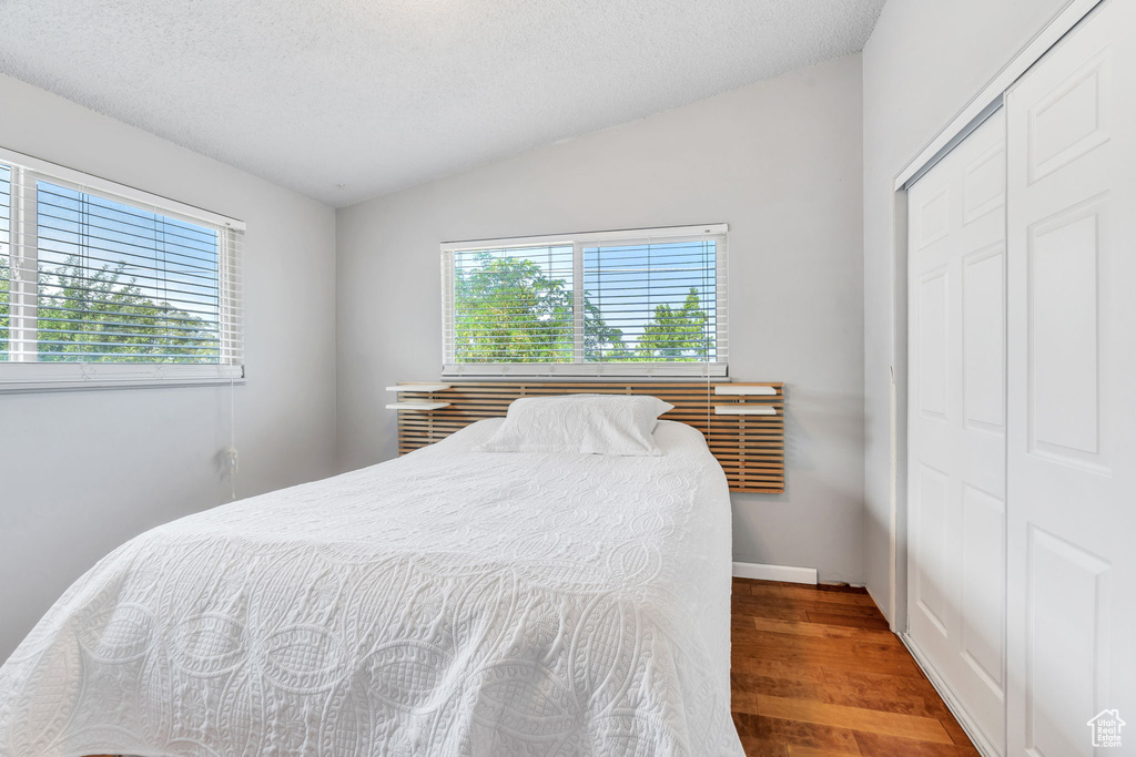 Bedroom featuring wood finished floors, multiple windows, a closet, lofted ceiling, and a textured ceiling