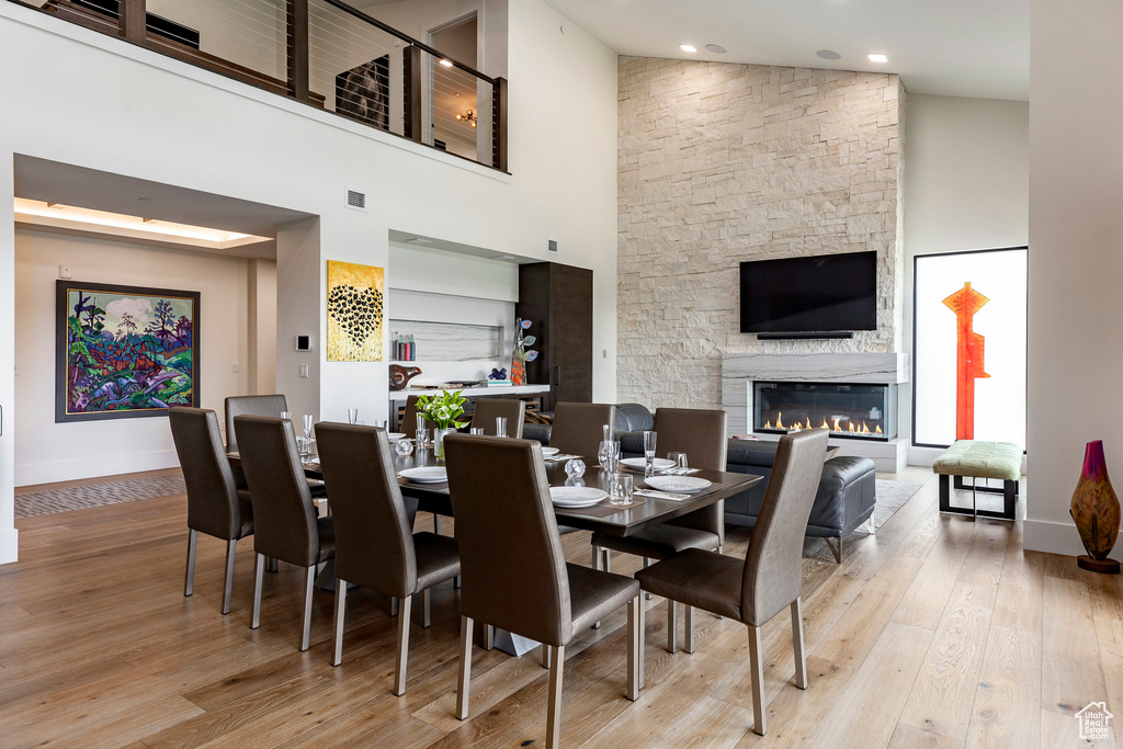 Dining space with a towering ceiling, a stone fireplace, and wood finished floors