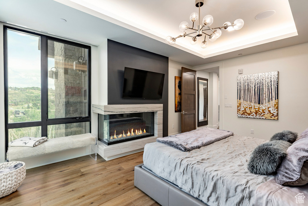 Bedroom featuring a chandelier, light wood-type flooring, a multi sided fireplace, and a raised ceiling