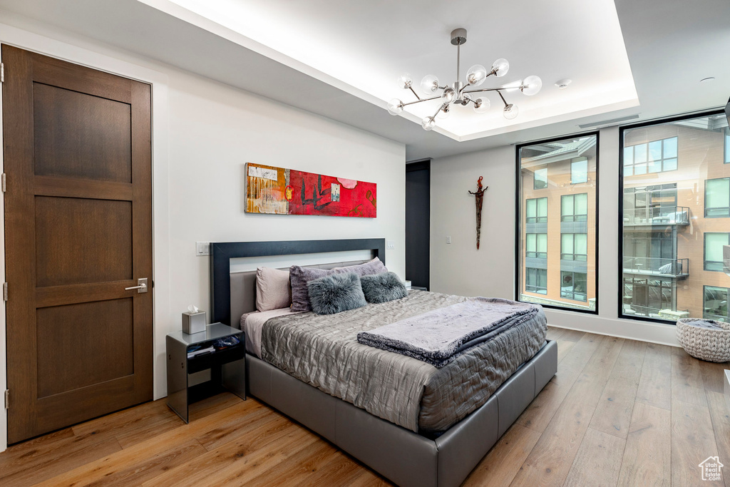 Bedroom with a chandelier, light wood-style flooring, and a raised ceiling
