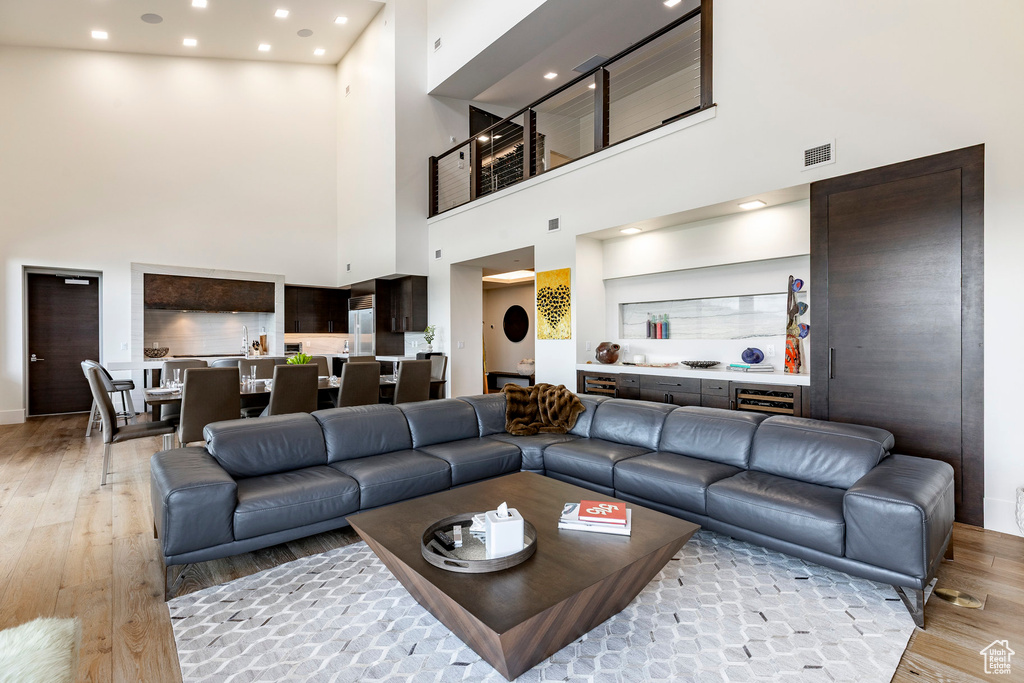 Living area with a towering ceiling, light wood-type flooring, recessed lighting, and beverage cooler
