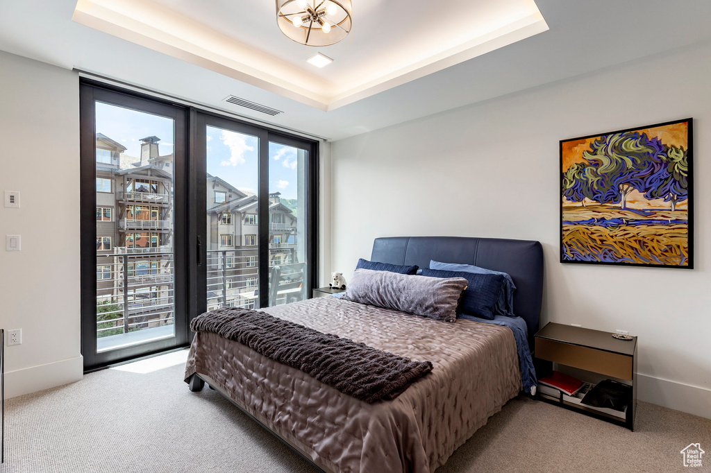 Carpeted bedroom featuring multiple windows, a raised ceiling, and access to exterior