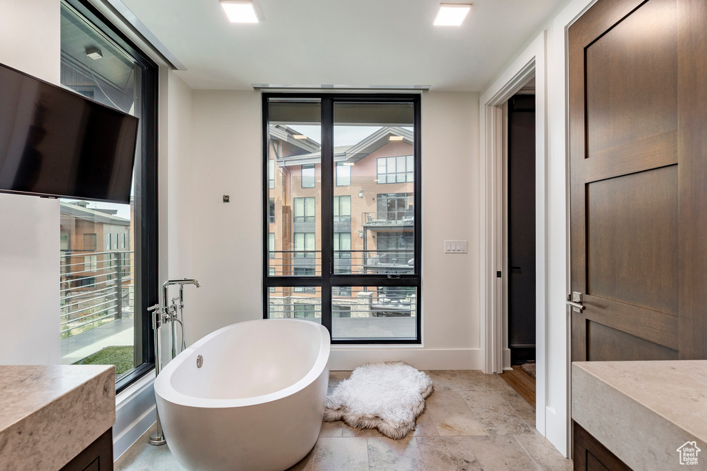 Bathroom featuring vanity, a soaking tub, healthy amount of natural light, and stone finish flooring