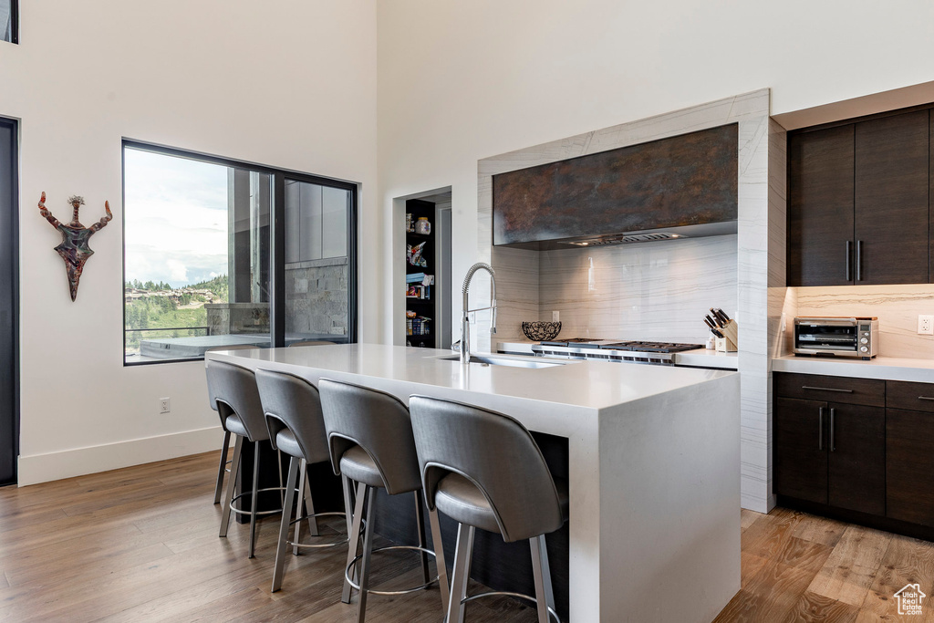 Kitchen featuring light countertops, backsplash, dark brown cabinets, light wood finished floors, and a kitchen bar