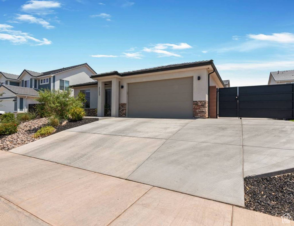 View of front of property featuring a garage, driveway, stone siding, and stucco siding