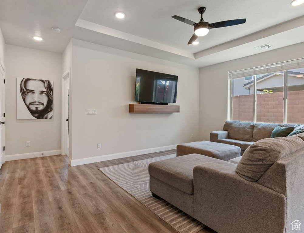 Living room with recessed lighting, wood finished floors, ceiling fan, and a tray ceiling