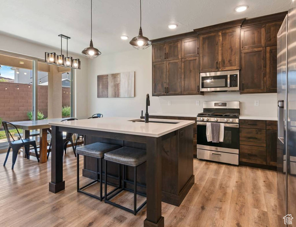 Kitchen with stainless steel appliances, light countertops, dark brown cabinets, light wood-style floors, and recessed lighting