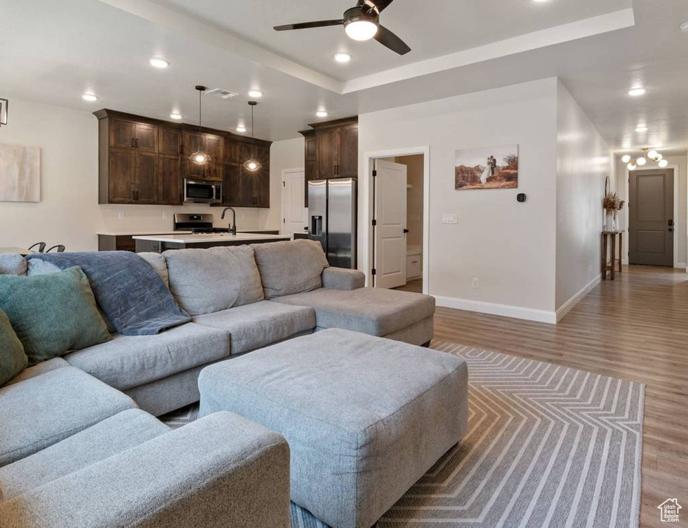 Living room featuring a ceiling fan, light wood-style flooring, recessed lighting, and a tray ceiling