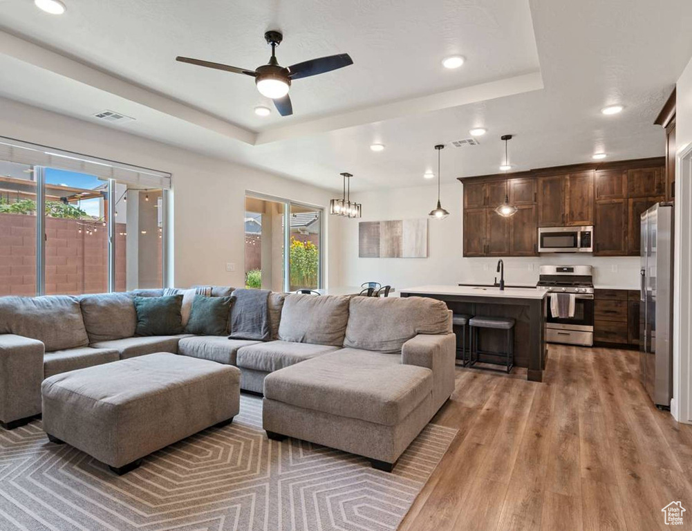 Living room with a raised ceiling, recessed lighting, light wood-style floors, and a ceiling fan