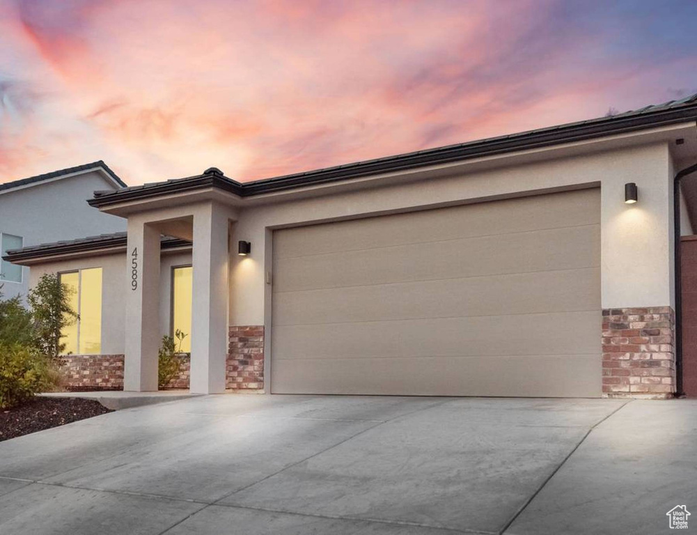 Prairie-style home featuring stone siding, driveway, an attached garage, and stucco siding