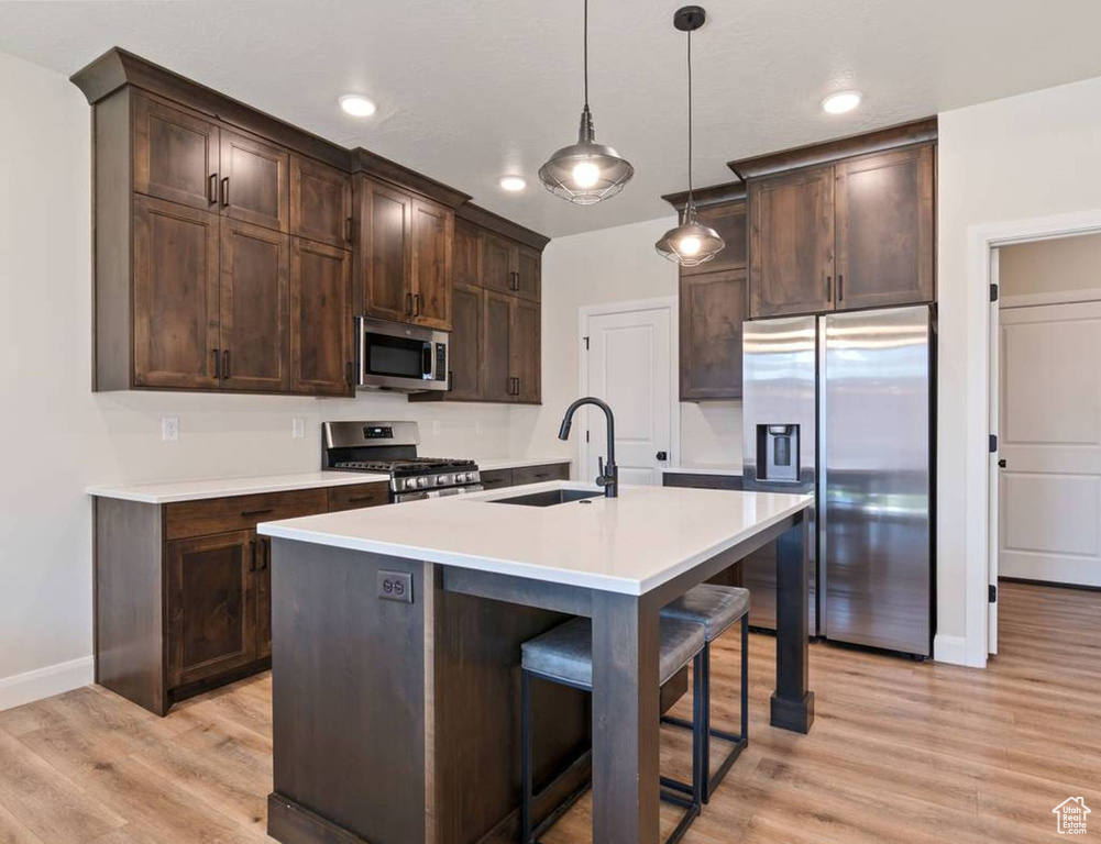Kitchen featuring stainless steel appliances, light wood-style flooring, dark brown cabinets, light countertops, and pendant lighting