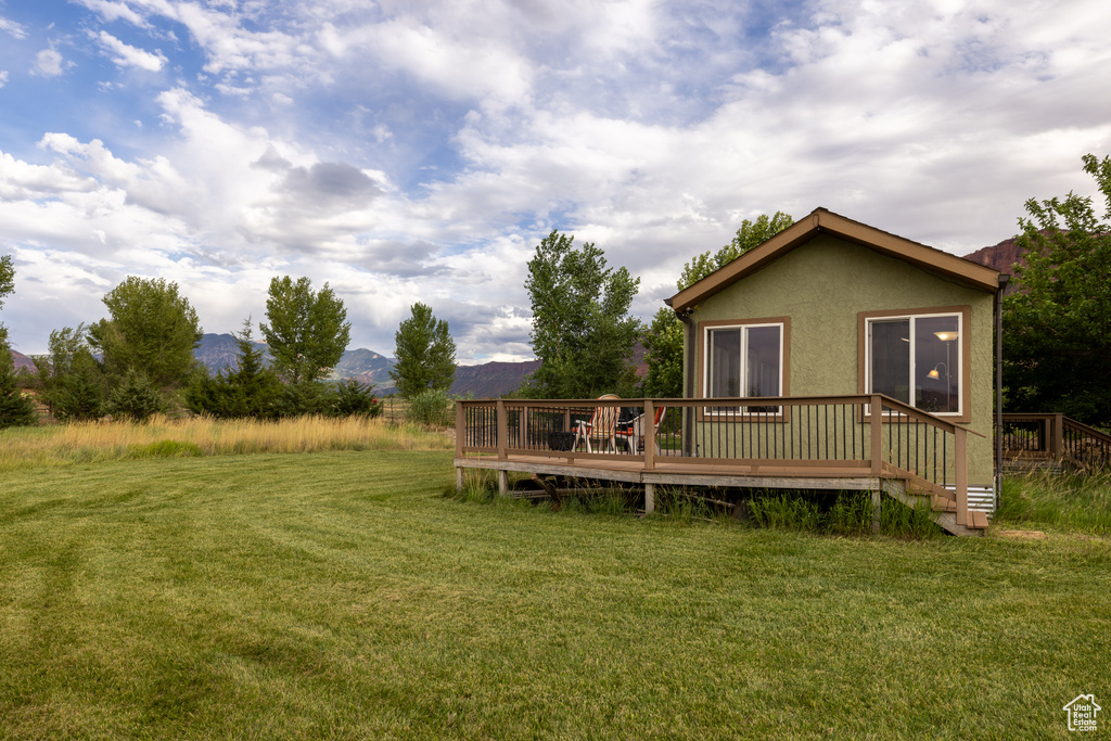 Back of house with a deck with mountain view, stucco siding, and a lawn