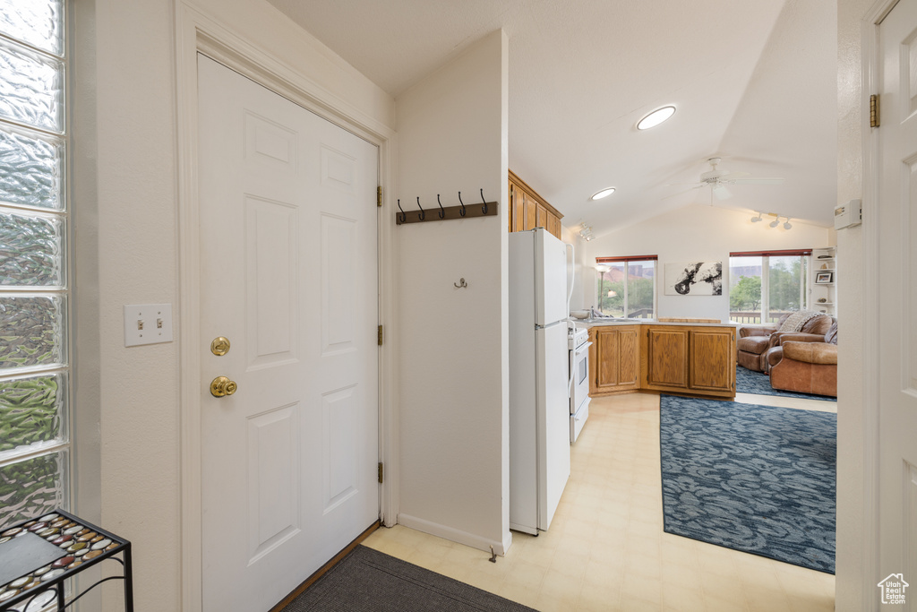 Kitchen featuring vaulted ceiling, a ceiling fan, light floors, brown cabinets, and white appliances