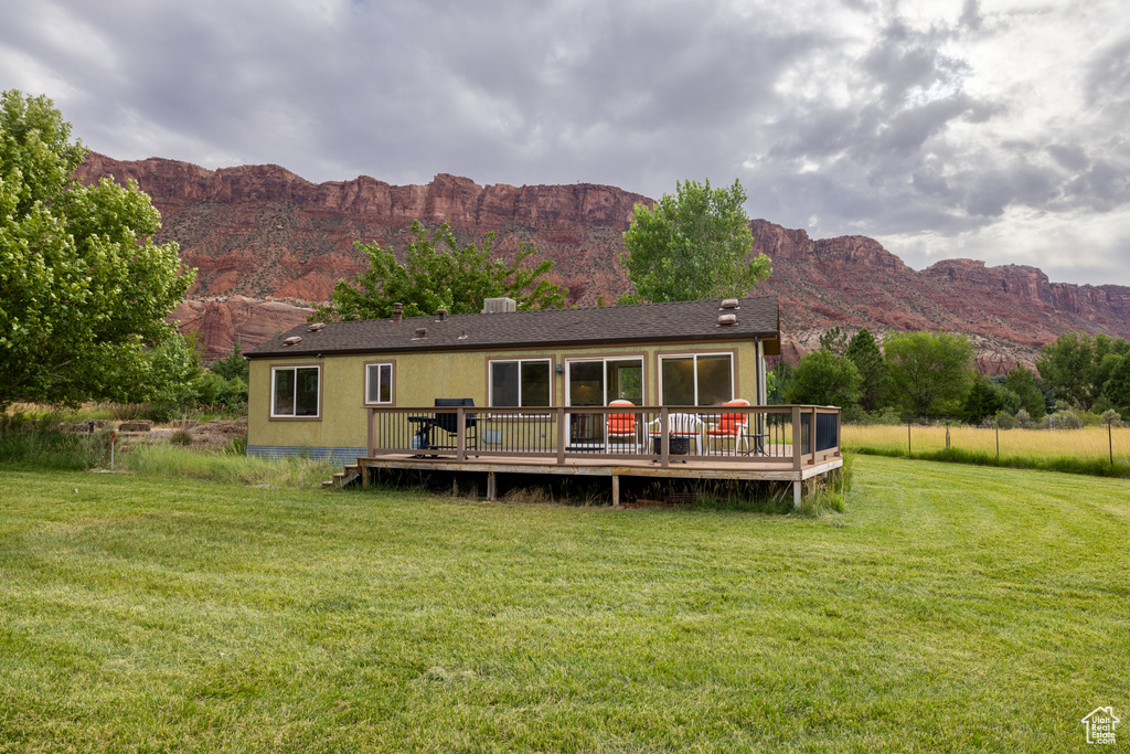 Back of property featuring a deck with mountain view, a lawn, and a shingled roof