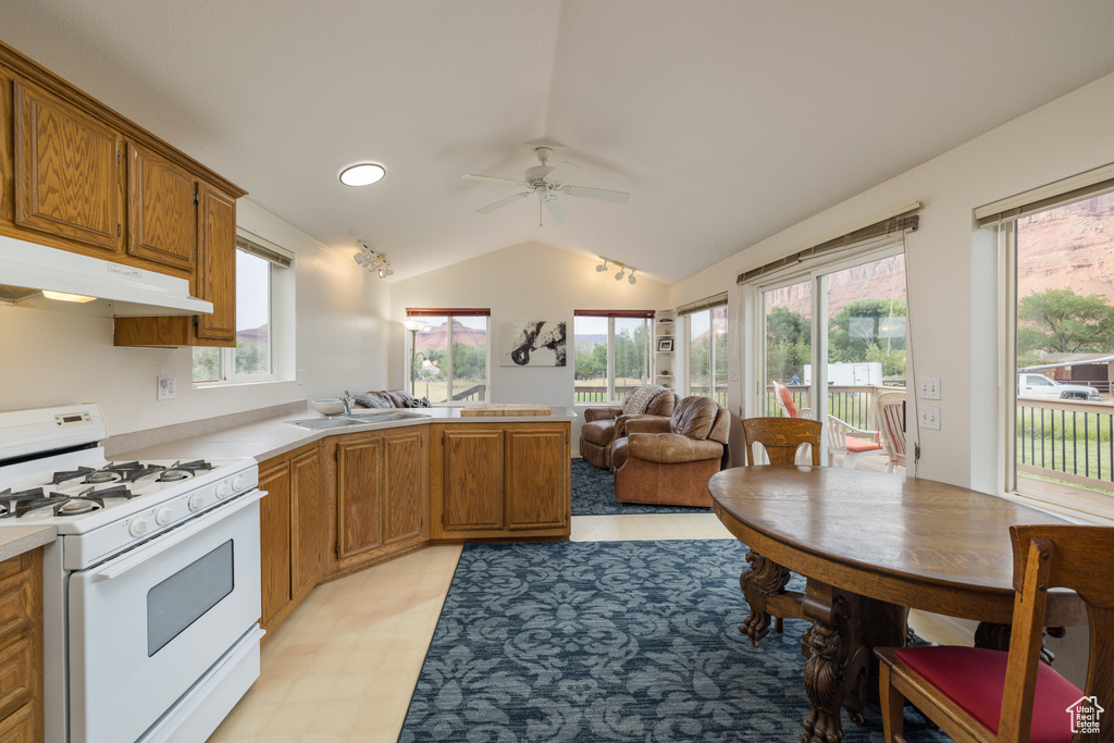Kitchen with white range with gas cooktop, a peninsula, lofted ceiling, light countertops, and ceiling fan