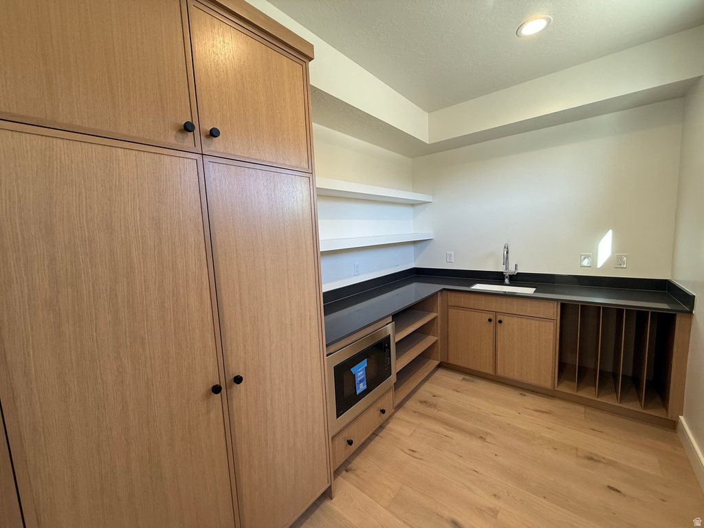 Kitchen with dark countertops, open shelves, light wood-type flooring, stainless steel microwave, and recessed lighting