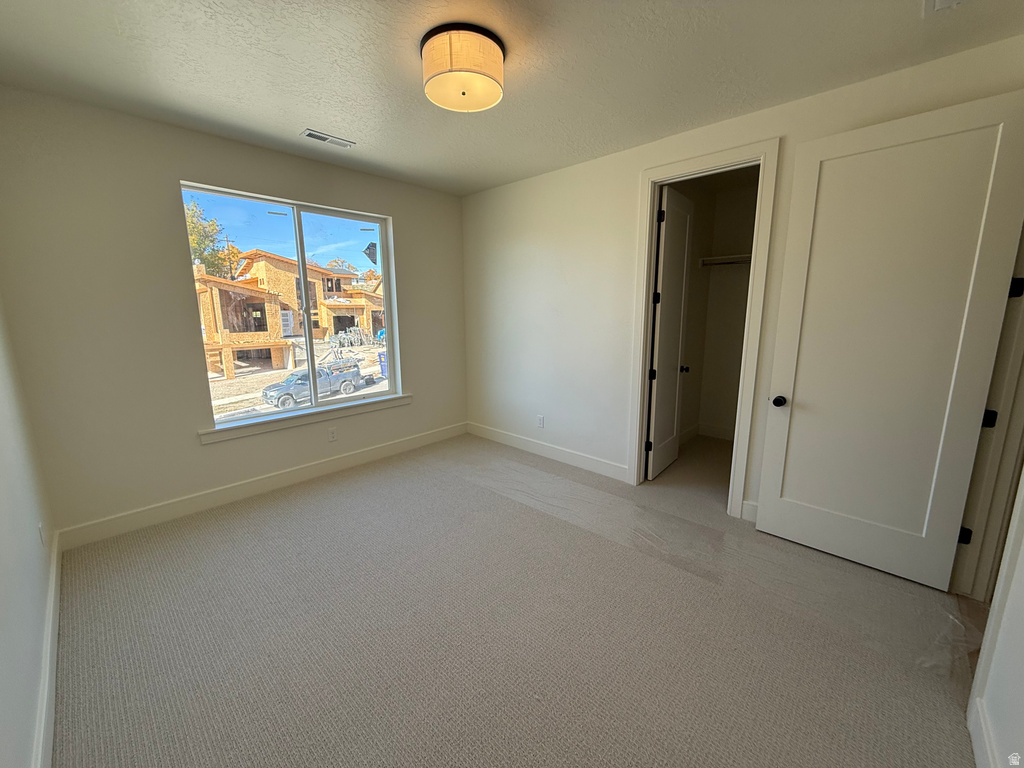 Unfurnished bedroom with carpet, a walk in closet, and a textured ceiling