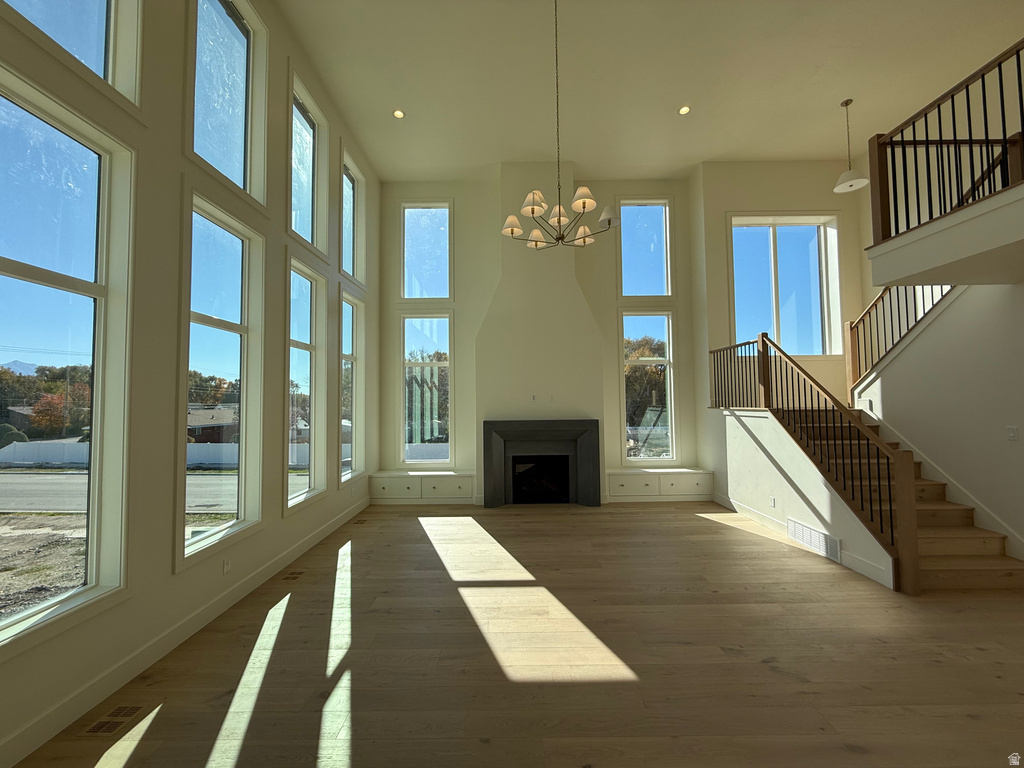 Unfurnished living room with a fireplace, wood finished floors, a towering ceiling, recessed lighting, and a chandelier