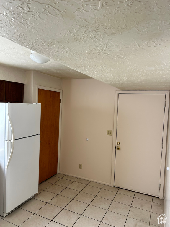 Kitchen featuring freestanding refrigerator, a textured ceiling, and light tile patterned floors