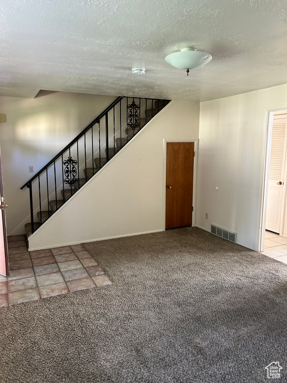 Unfurnished living room featuring stairway, carpet flooring, and a textured ceiling
