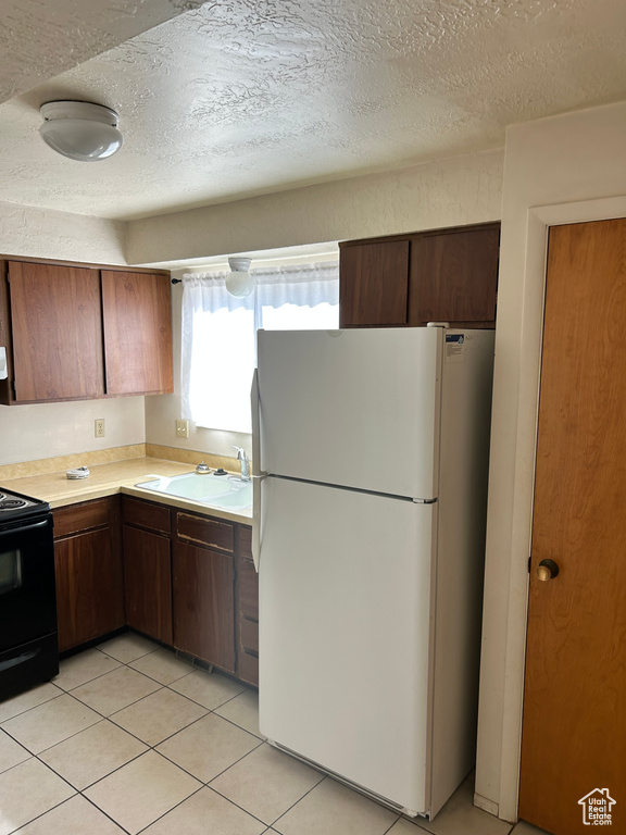 Kitchen with freestanding refrigerator, light countertops, black range with electric cooktop, a textured ceiling, and light tile patterned flooring