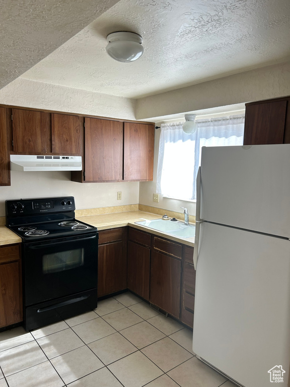 Kitchen featuring freestanding refrigerator, electric range, light countertops, light tile patterned floors, and a textured ceiling
