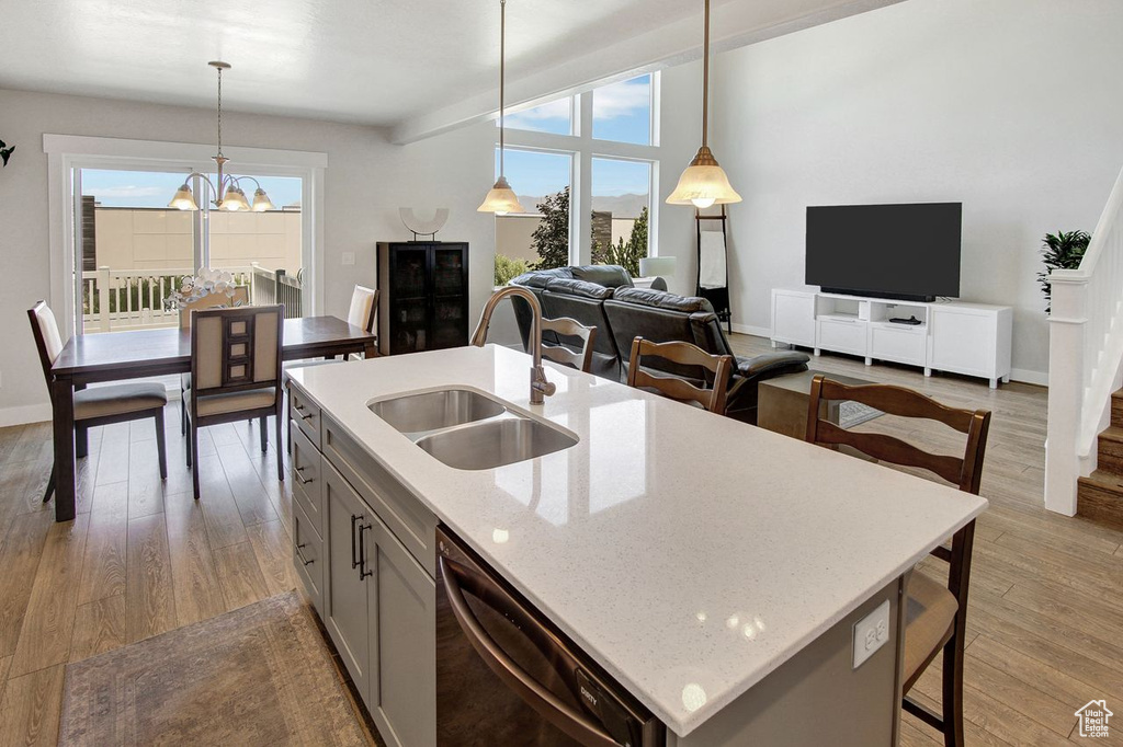Kitchen with dishwasher, pendant lighting, light wood-style flooring, a chandelier, and a center island with sink