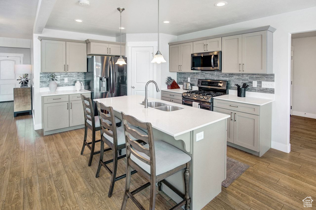 Kitchen featuring gray cabinetry, appliances with stainless steel finishes, decorative backsplash, a kitchen bar, and light wood-type flooring